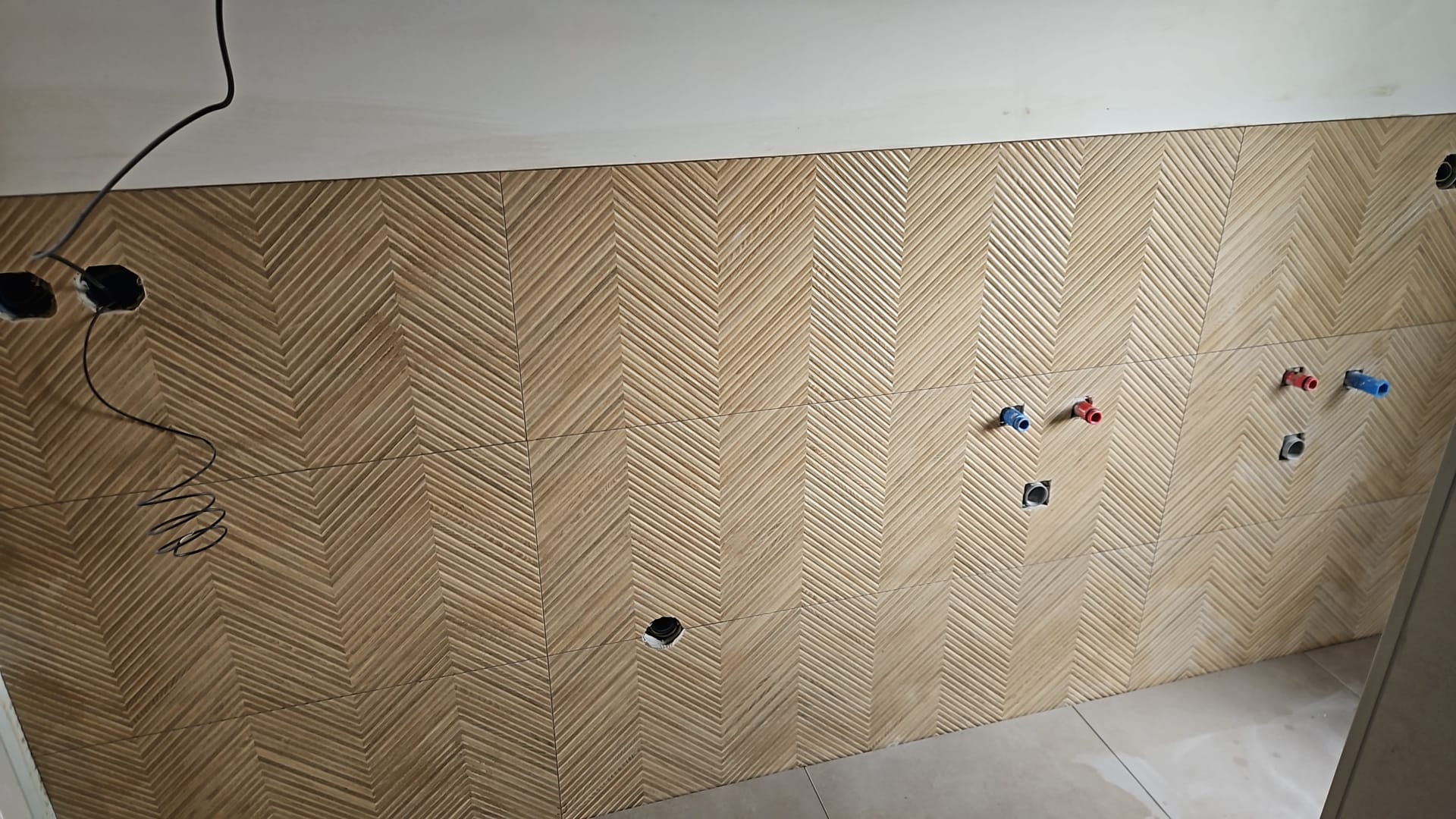 Betegelde badkamerwand met visgraat reliëftegels en leidingwerk voor een dubbele wastafel (foto 2 van 3)