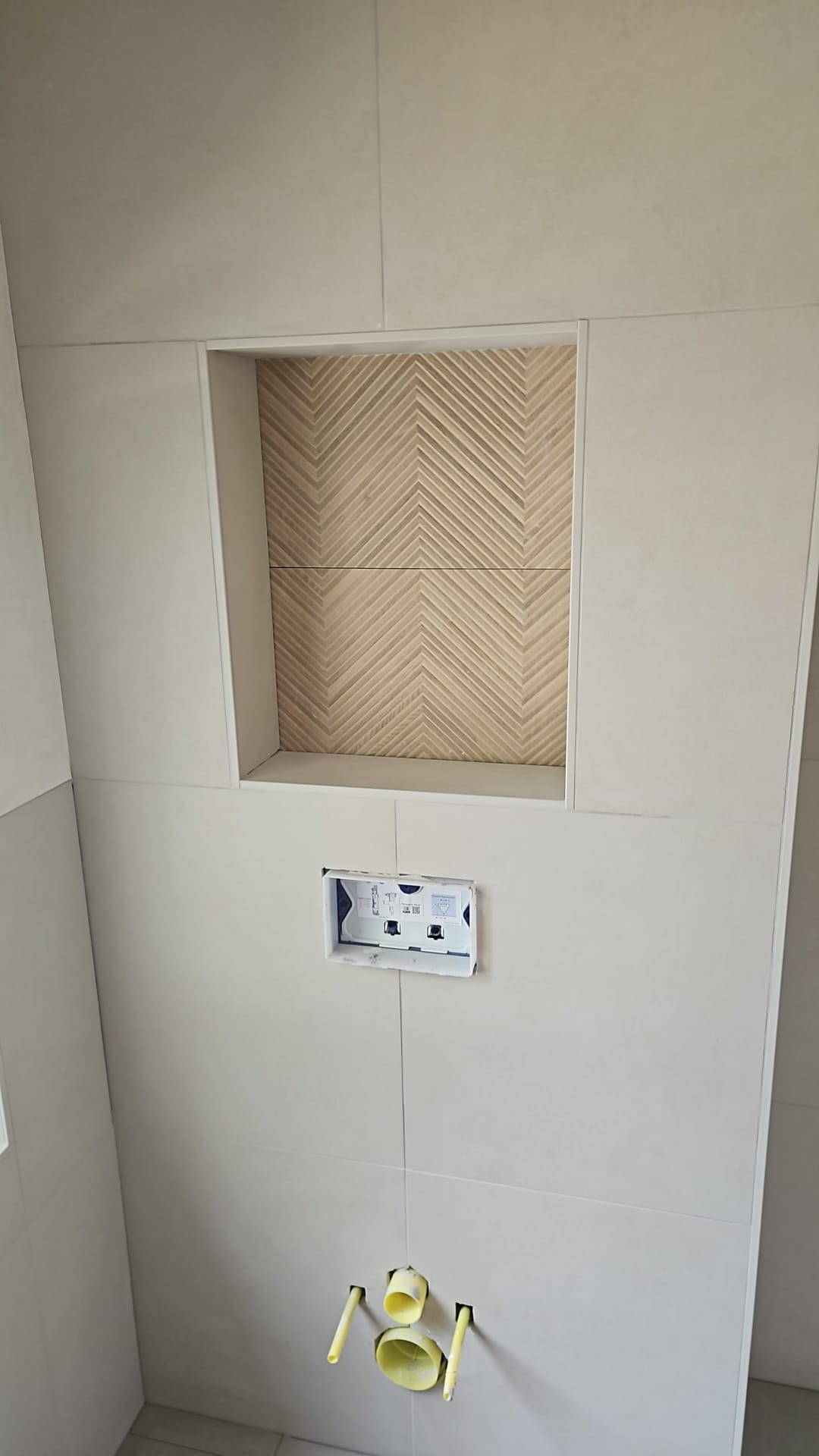 Inbouwtoilet met strakke beige wandtegels en een nis met visgraat reliëftegels (foto 1 van 3)