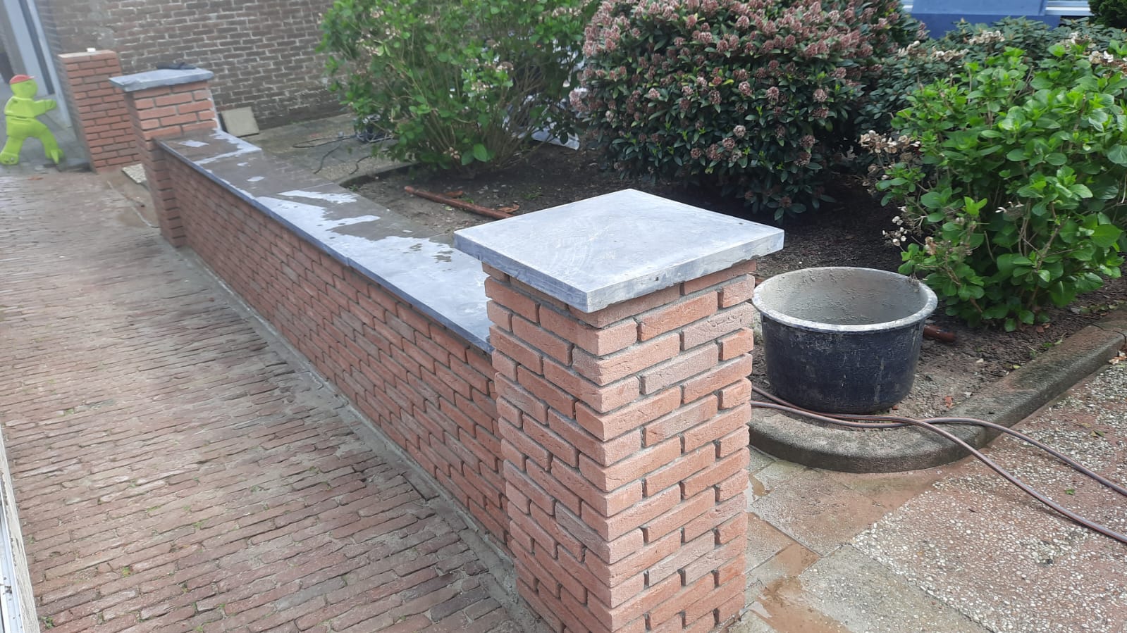 Laag tuinmuurtje met gemetselde kolommen, afgewerkt met grijze natuurstenen afdekplaten (foto 2 van 3)